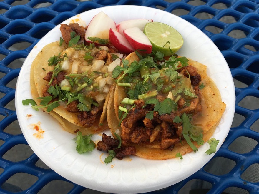 Two pork street tacos on doubled corn tortillas with onion, cilantro and salsa verde, lime and radish on the side, photographed from above.
